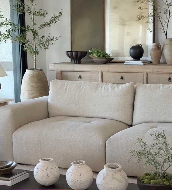 A linen sofa beside hand-shaped clay vases in warm afternoon light
